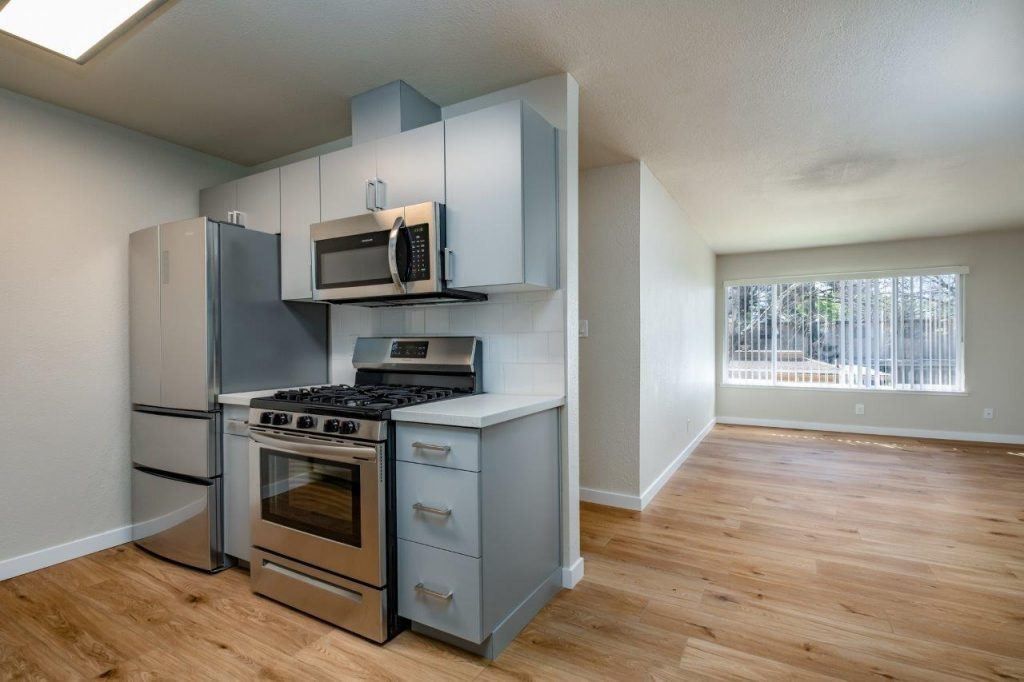 Small kitchen and open living area with stainless appliances, light gray cabinets, and wood floors