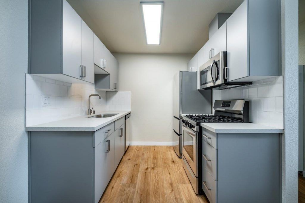 Modern galley kitchen with white cabinets, gray accents, stainless appliances, and wood flooring