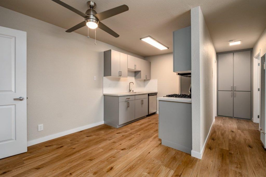 Bright kitchen and dining area with wood floors, white cabinets, ceiling fan, and hallway view