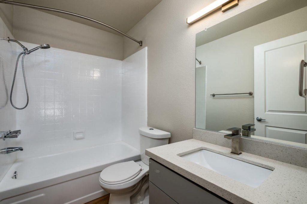 Modern white bathroom with tub-shower, toilet, vanity, and large mirror