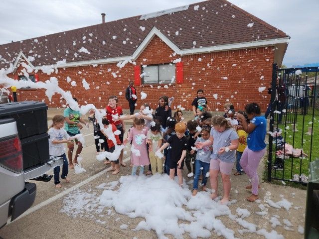 A group of children are playing with foam in front of a brick building