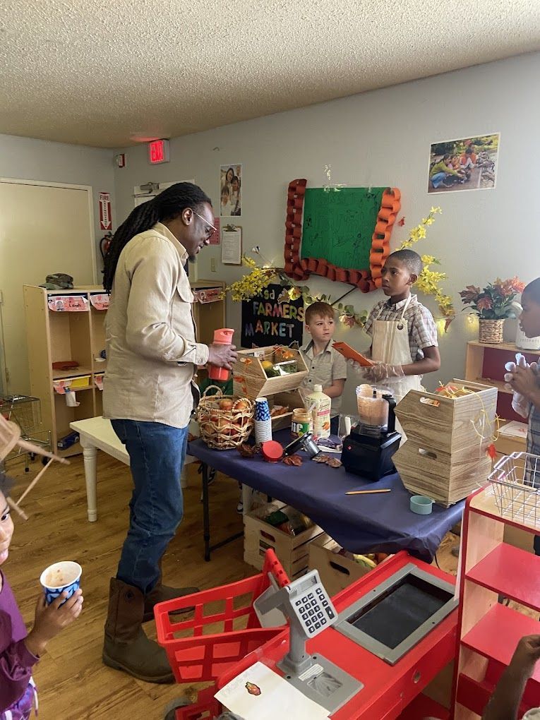 A man is standing in front of a table in a room with children.