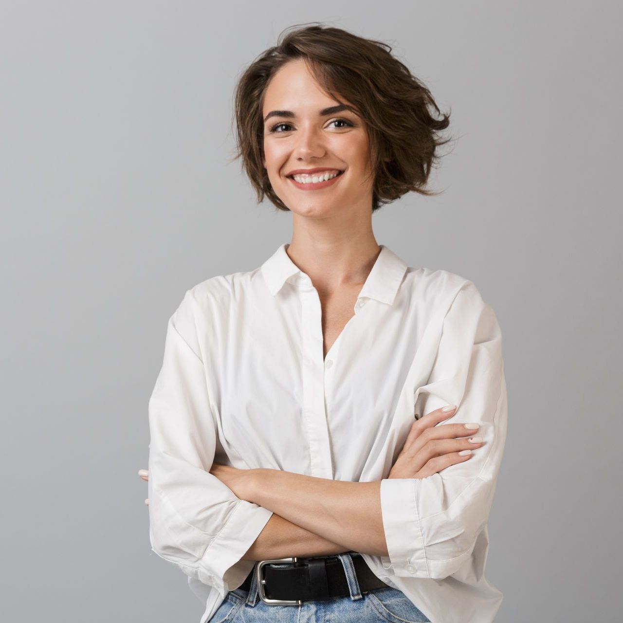 A woman in a white shirt and jeans is smiling with her arms crossed.