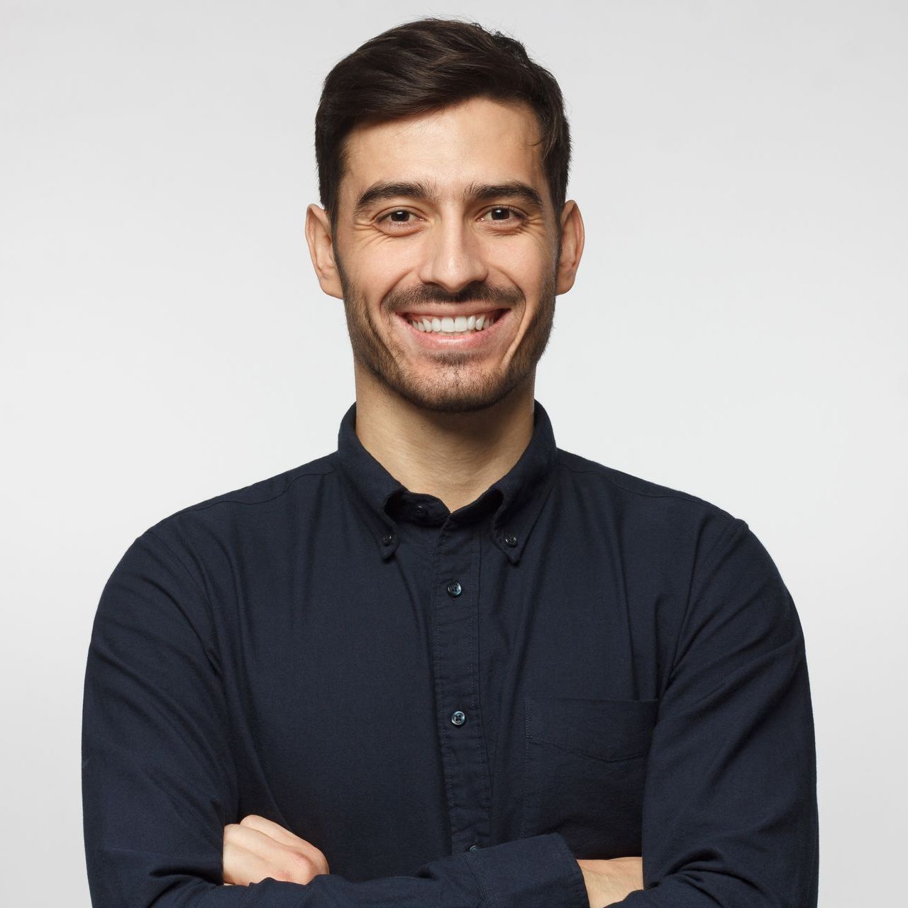 A man in a blue shirt is smiling with his arms crossed