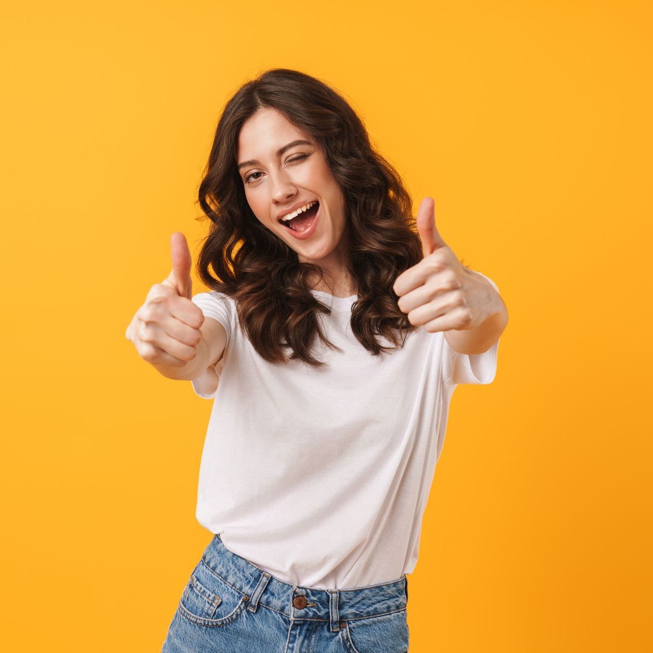 A young woman is giving a thumbs up sign over a yellow background.