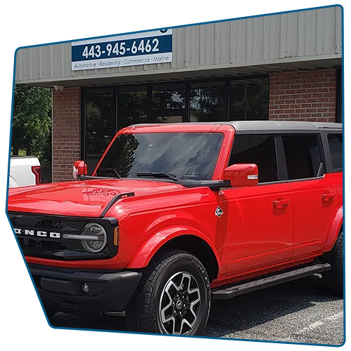 Red Ford Bronco parked in front of a brick building with a business sign above the door.
