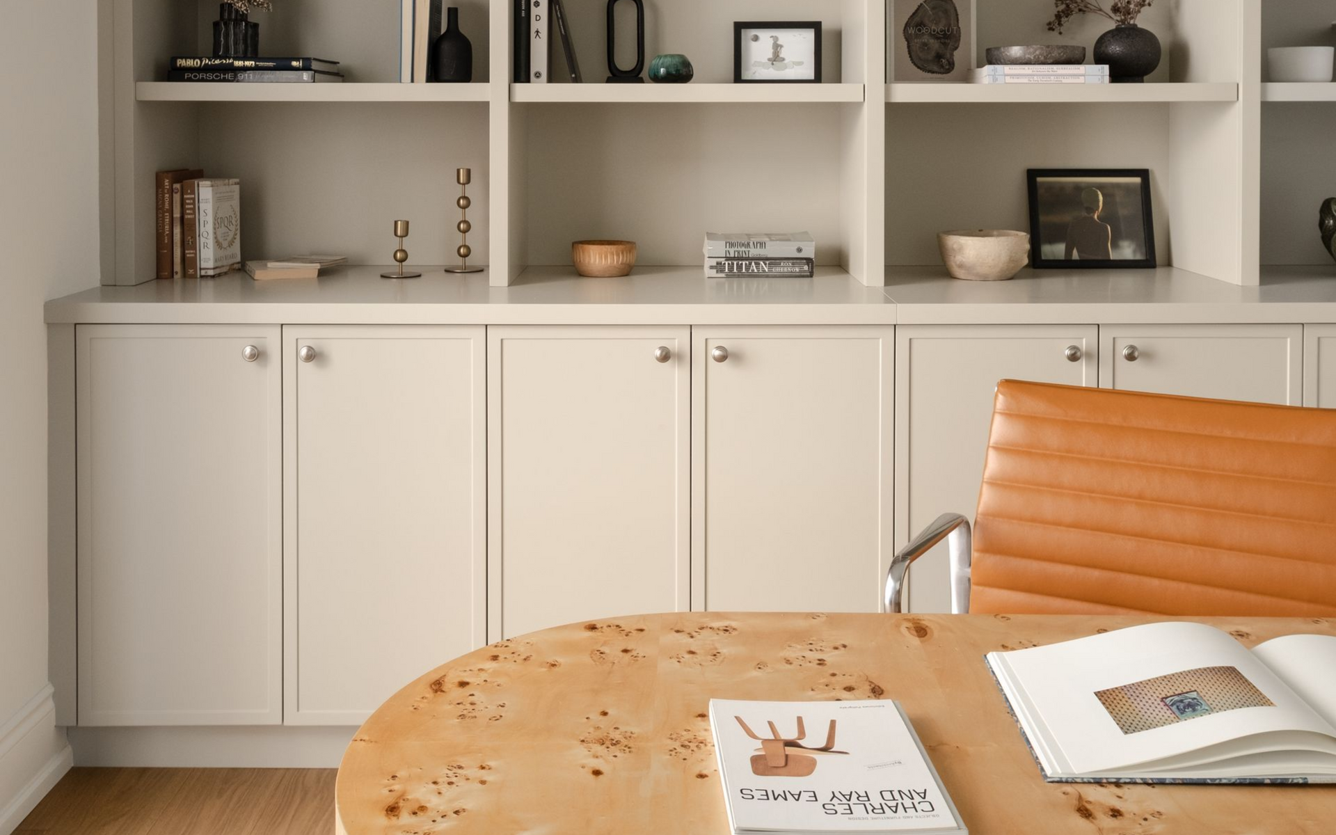 Room with white cabinets, shelves, and a round wooden table with open books and an brown leather chair.