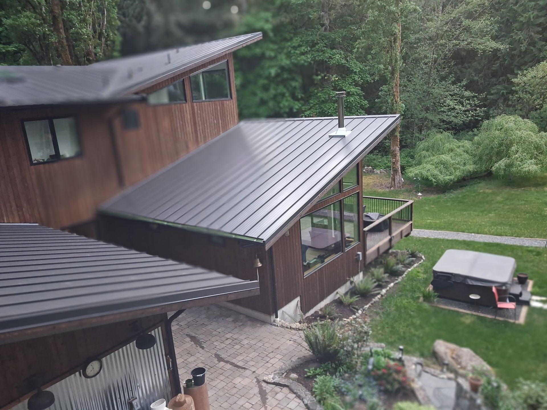 Wooden house with metal roofs beside a grassy yard and picnic table, surrounded by trees