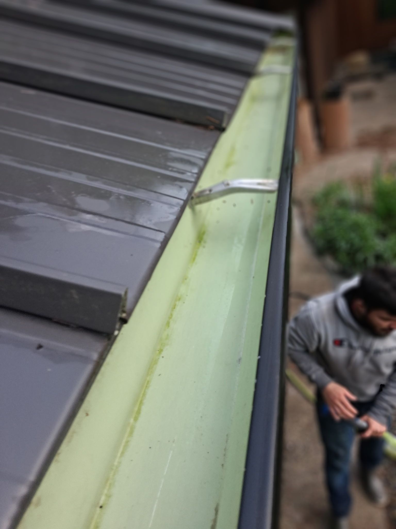 Close-up of a metal roof edge with a gutter and a worker using tools below