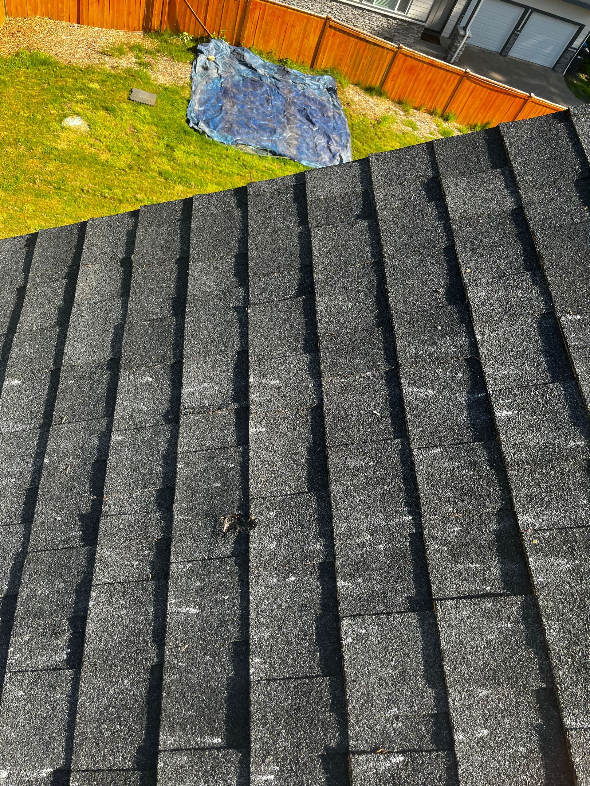 Dark gray shingled roof in the foreground with a grassy yard and orange fence behind it