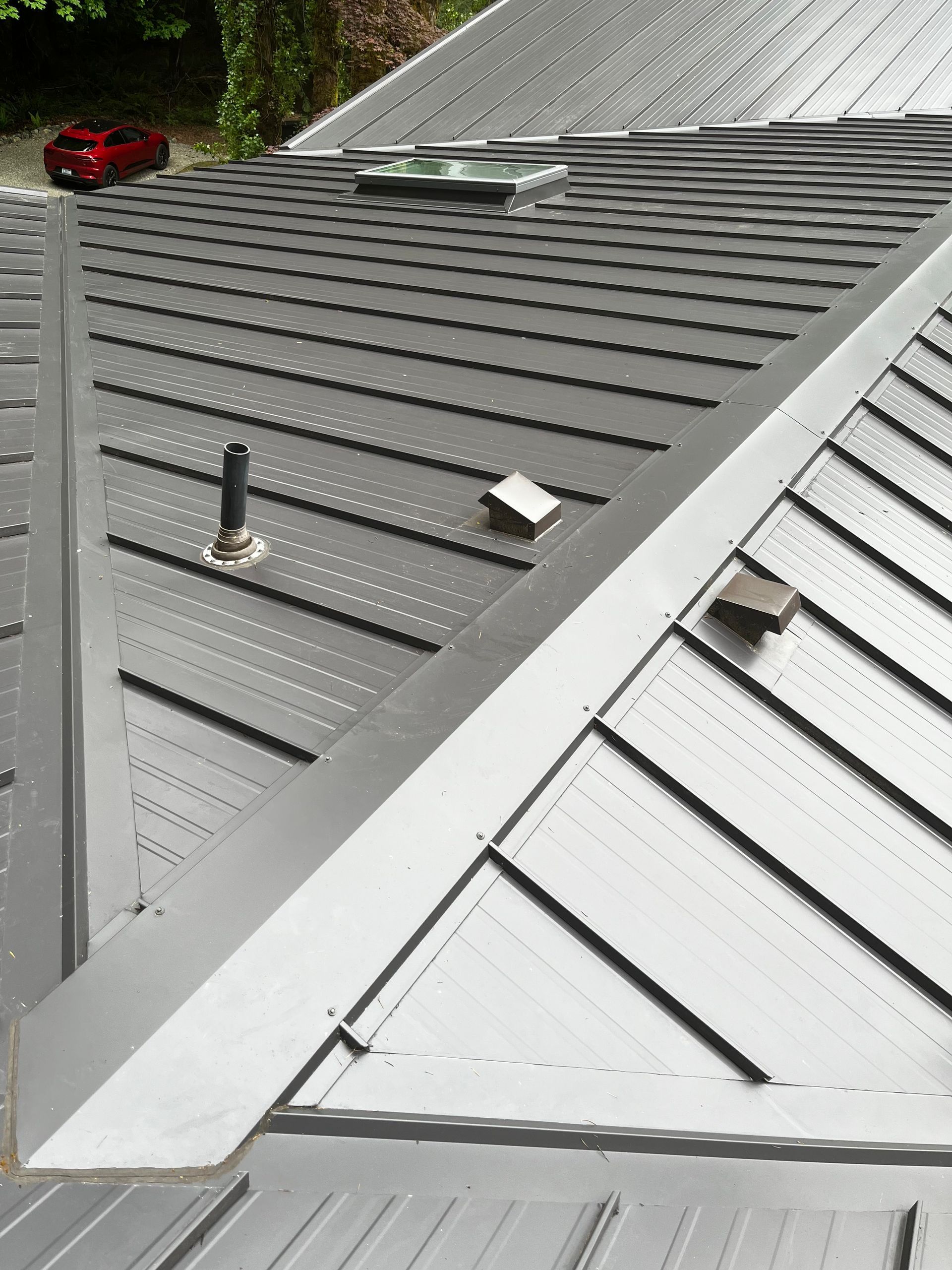Gray metal roof with skylights, vents, and a silver roof edge on a sloped house