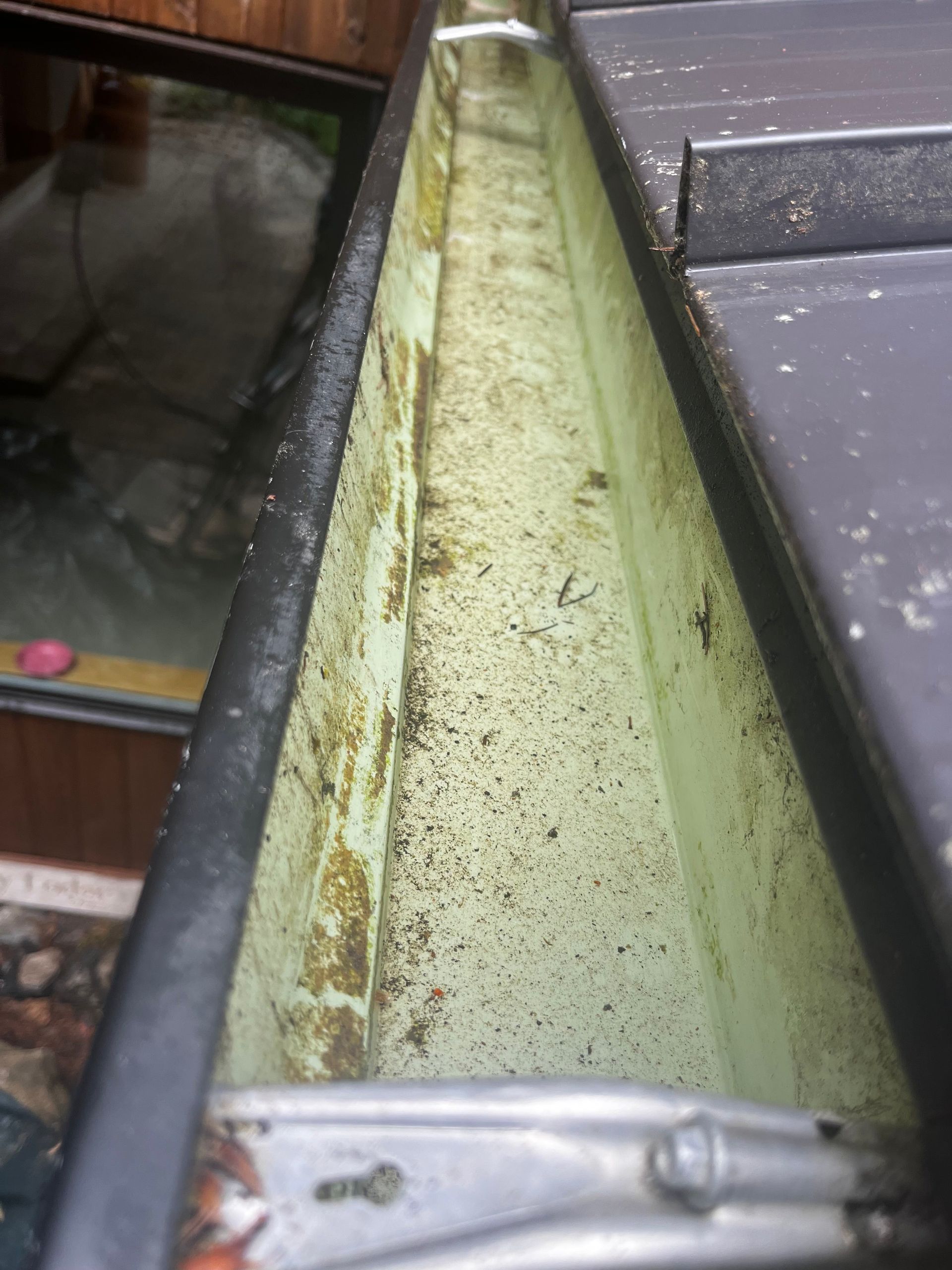 Close-up of a dirty green metal gutter or channel with debris and water stains outdoors