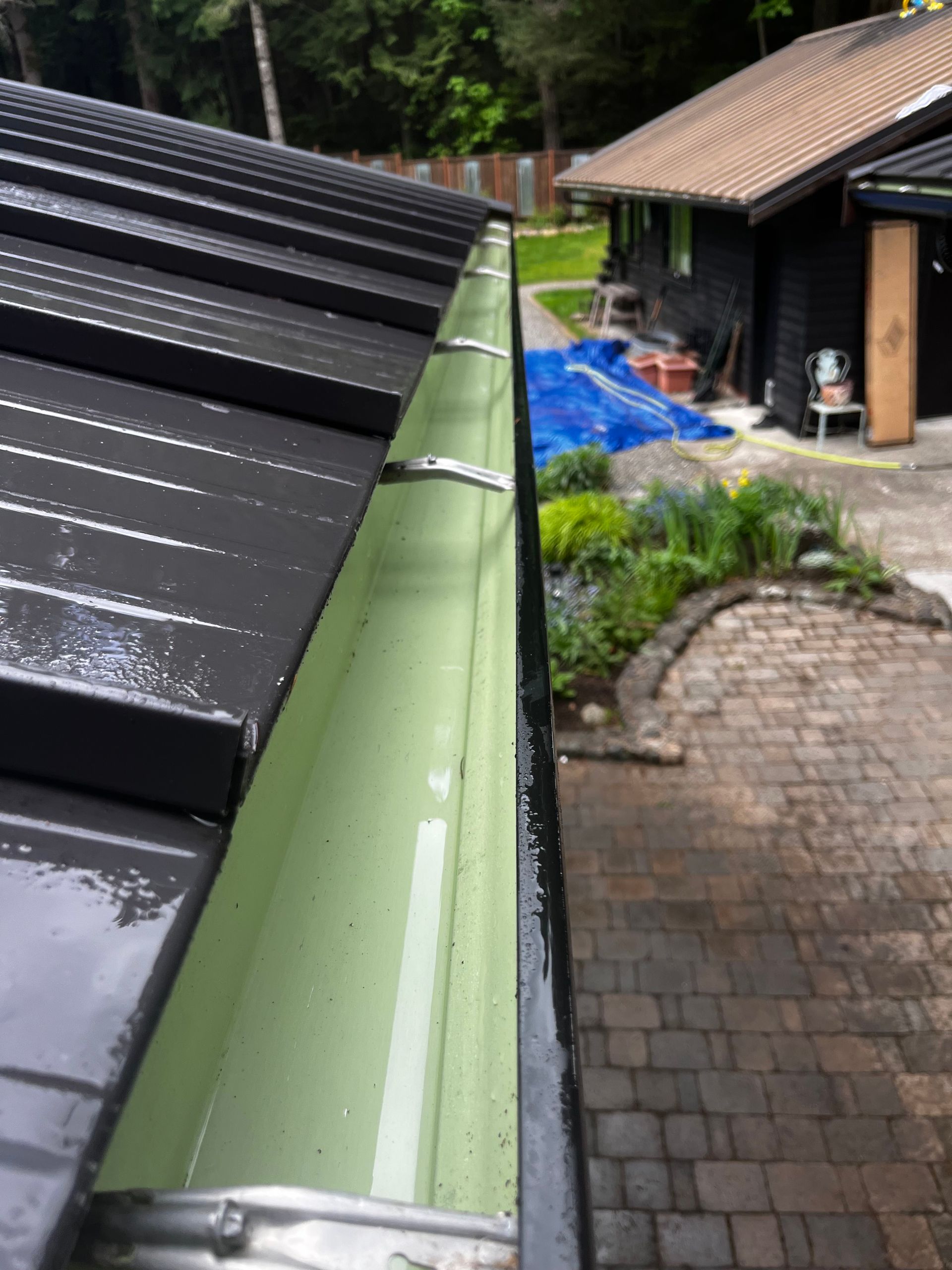Rainwater gutter beside wet black roof and brick patio near a house under repair