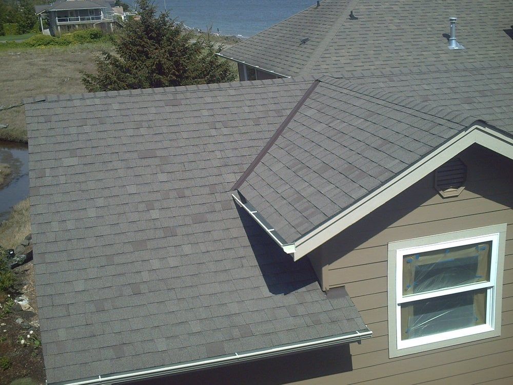 Gray shingled house roof with a dormer window and chimney, viewed from above.