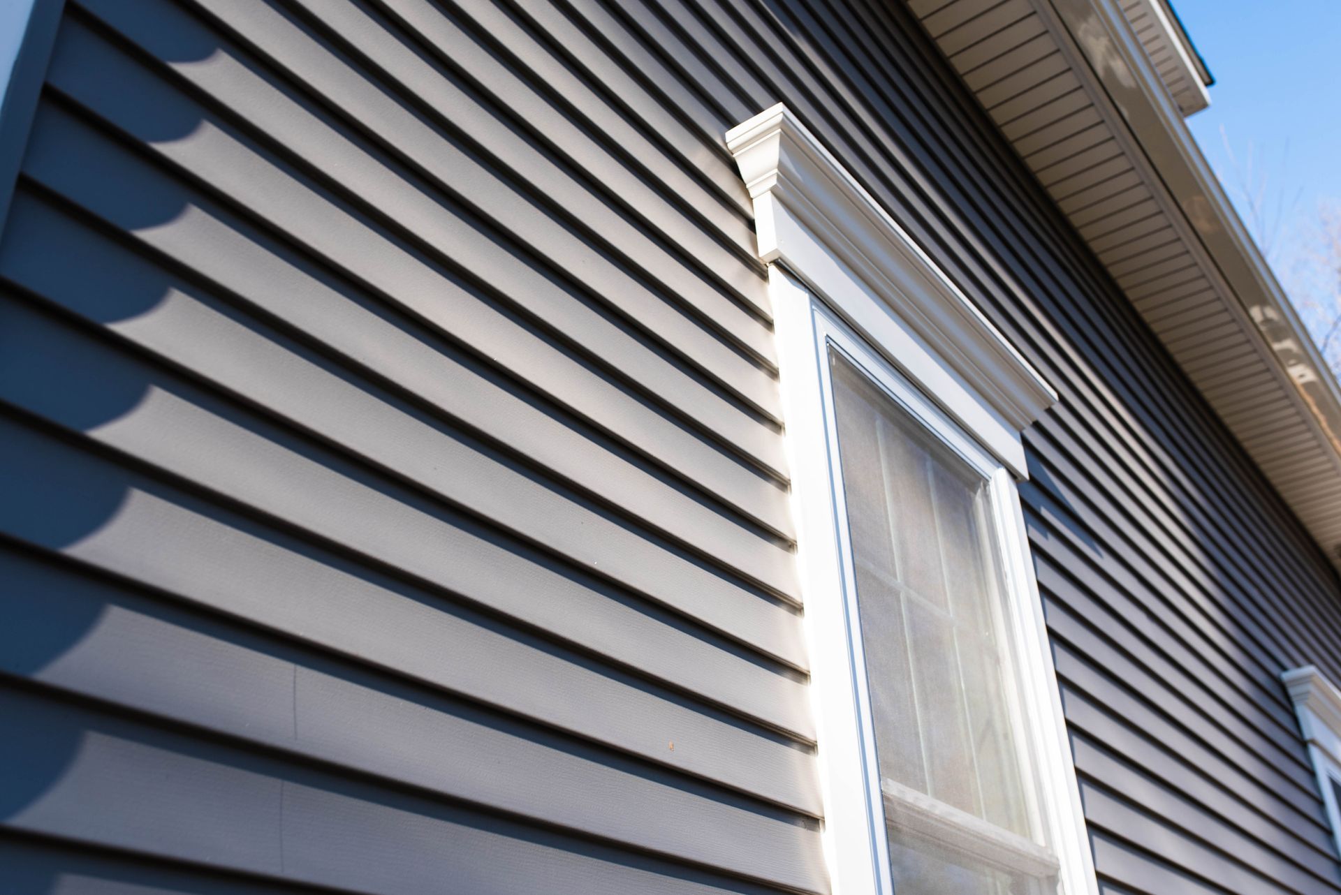 Gray house siding with white-trimmed window and eaves viewed from below