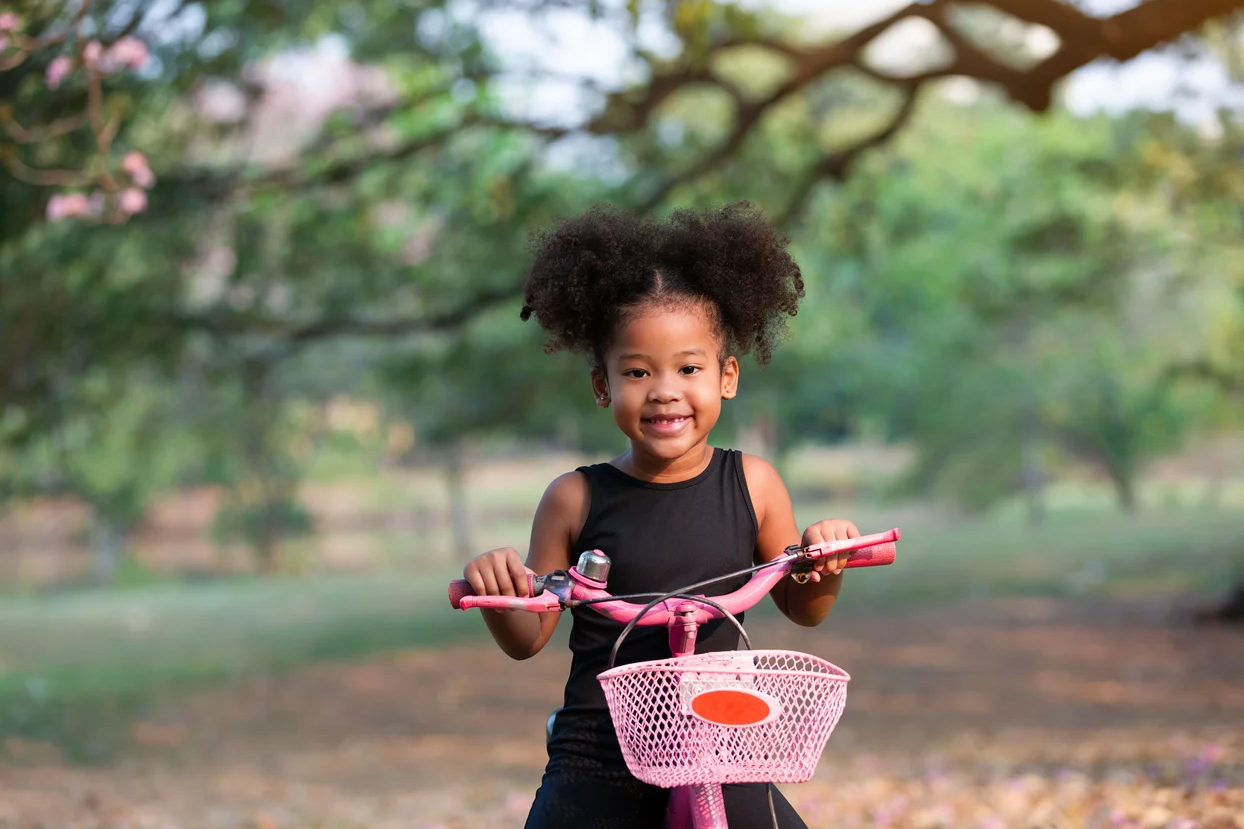 A little girl is riding a pink bicycle in a park.