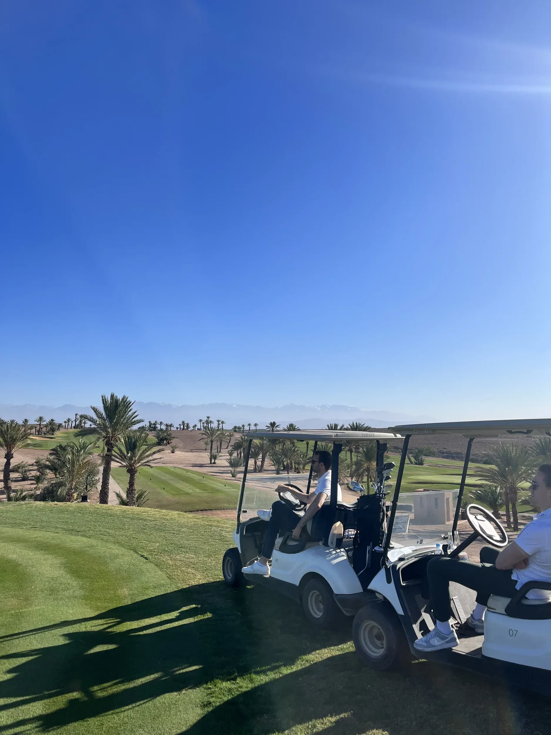 Two golf carts are parked on a golf course on a sunny day.