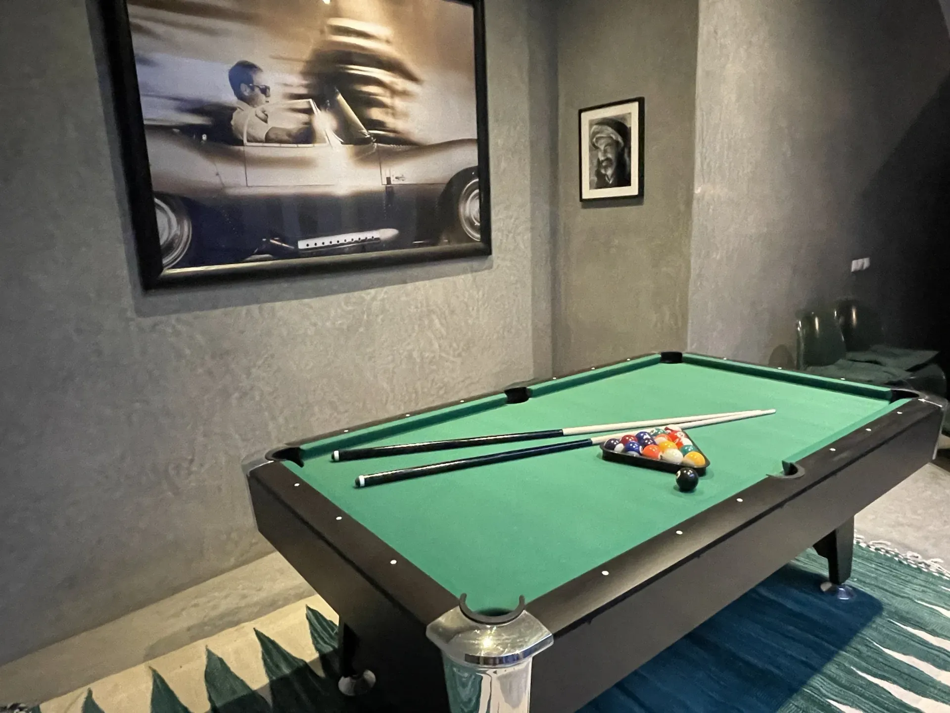 A pool table with a picture of a car on the wall above it.