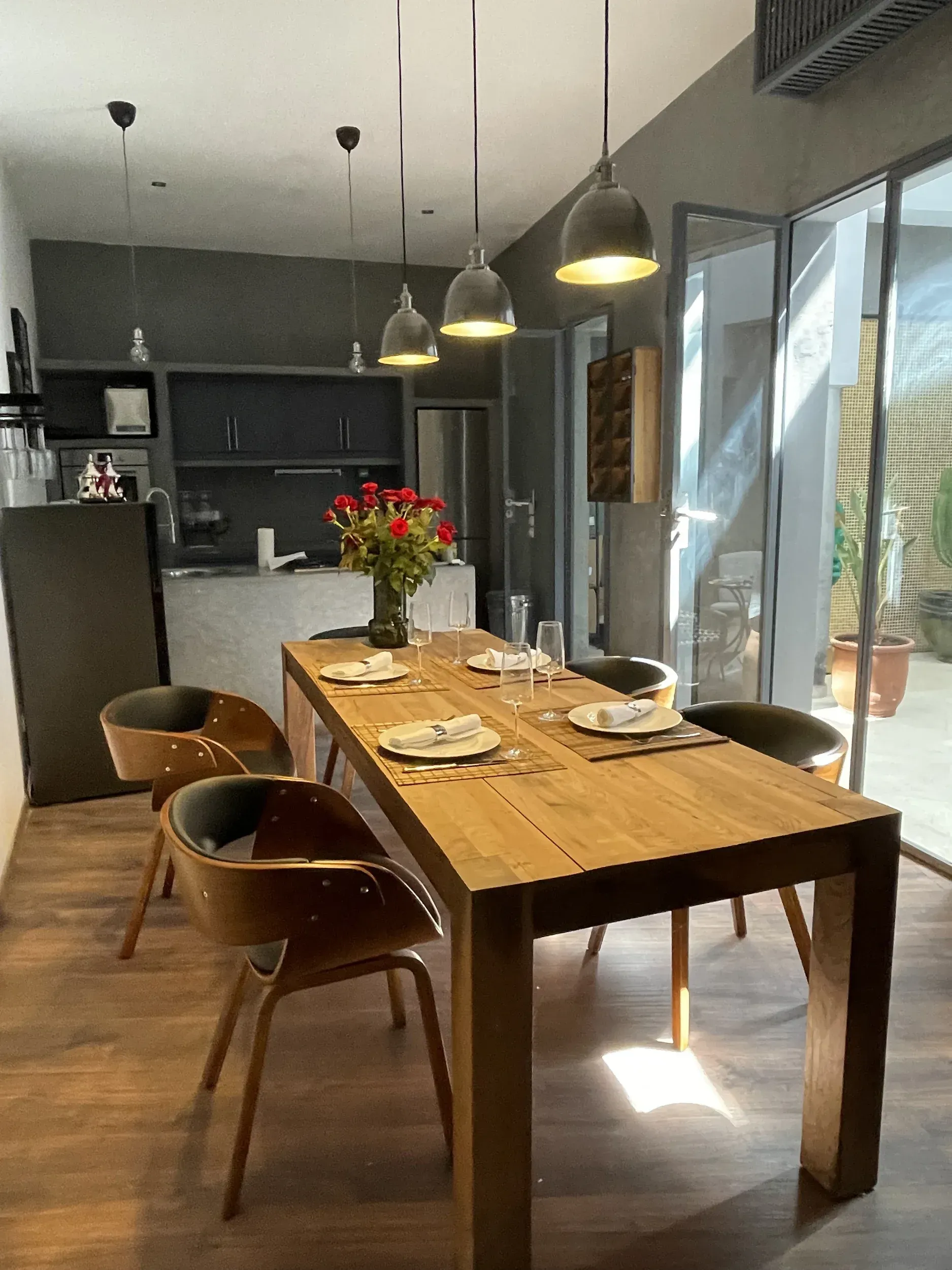 A dining room with a wooden table and chairs and a vase of flowers on the table.