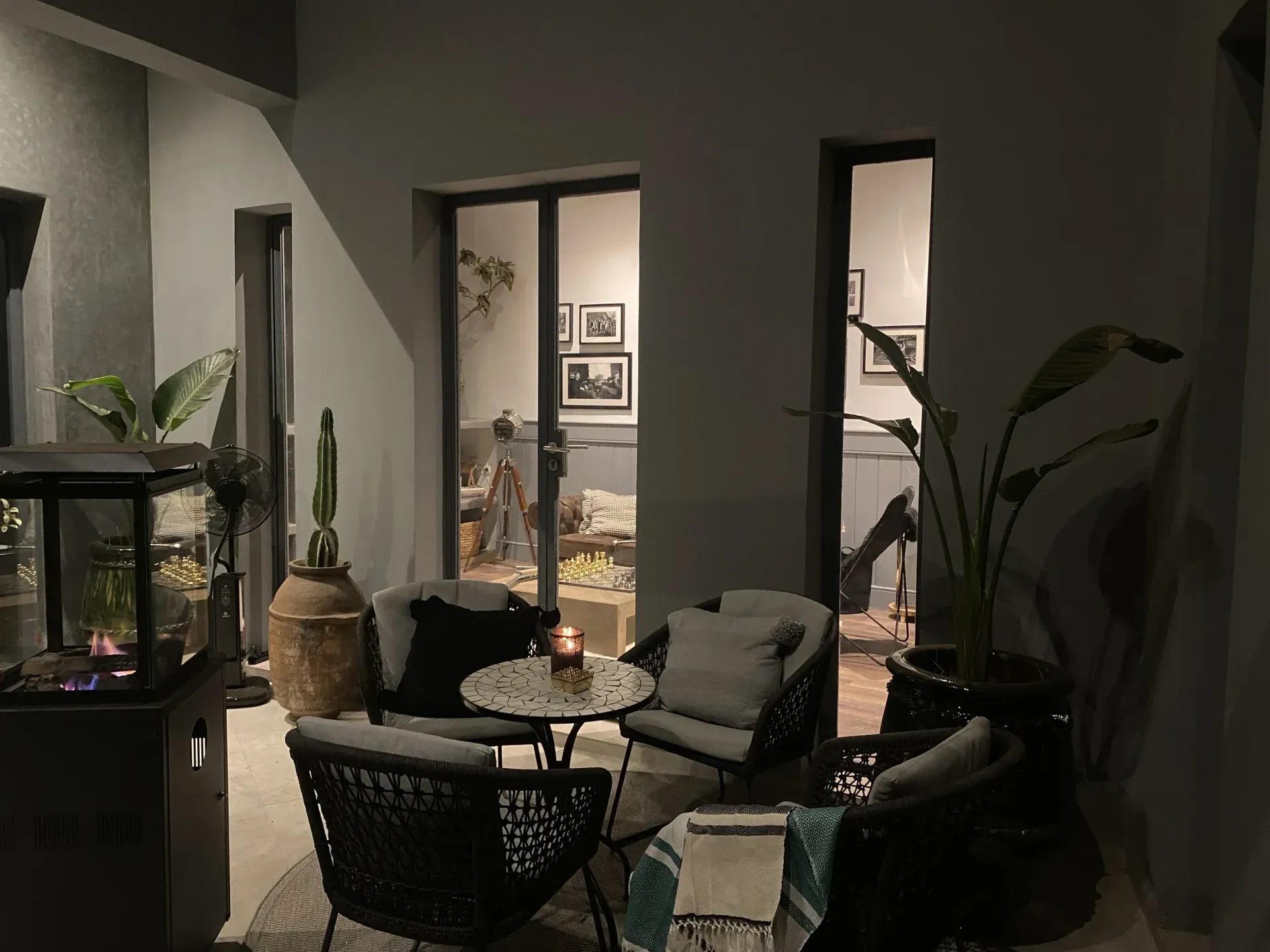 A patio with chairs , a table and a fireplace at night.
