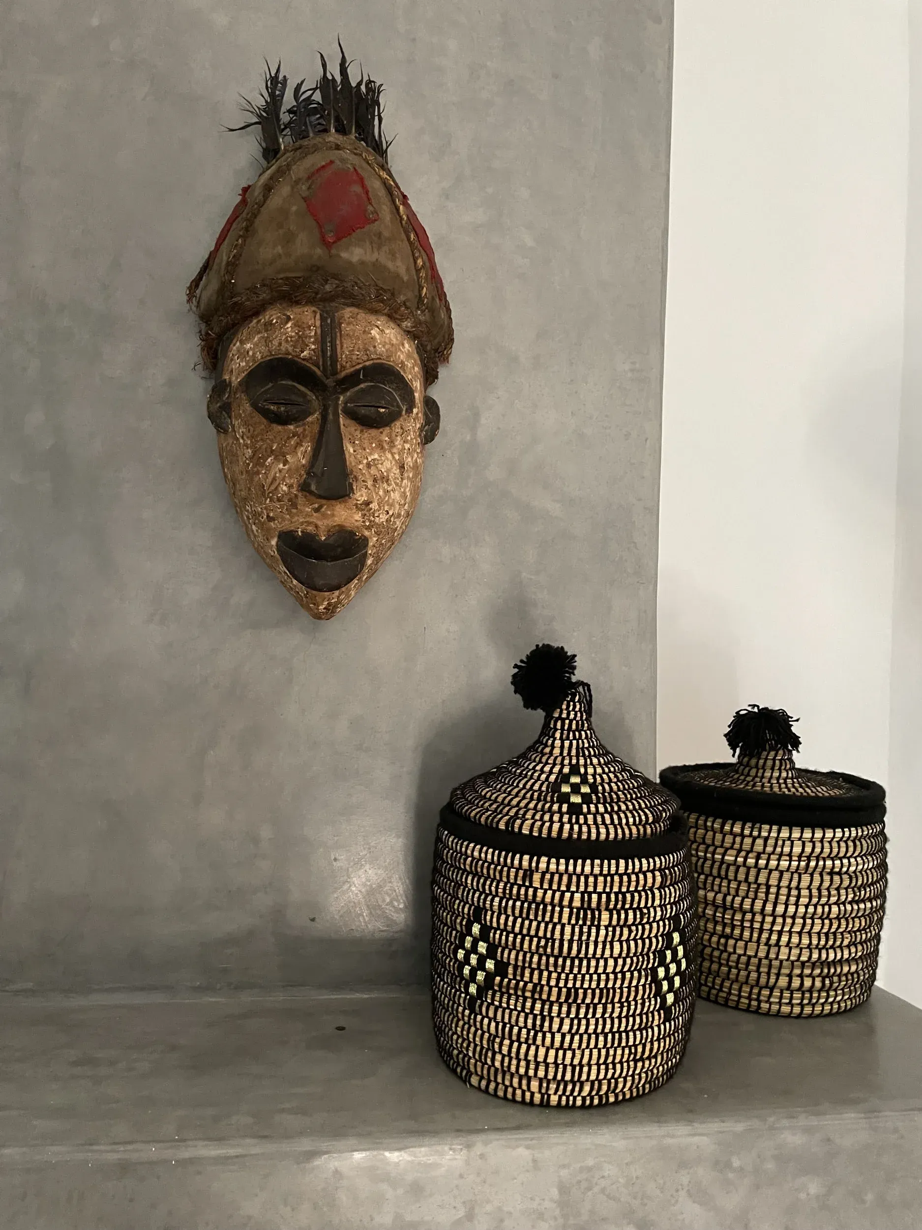 A wooden mask is hanging on a wall next to two baskets.