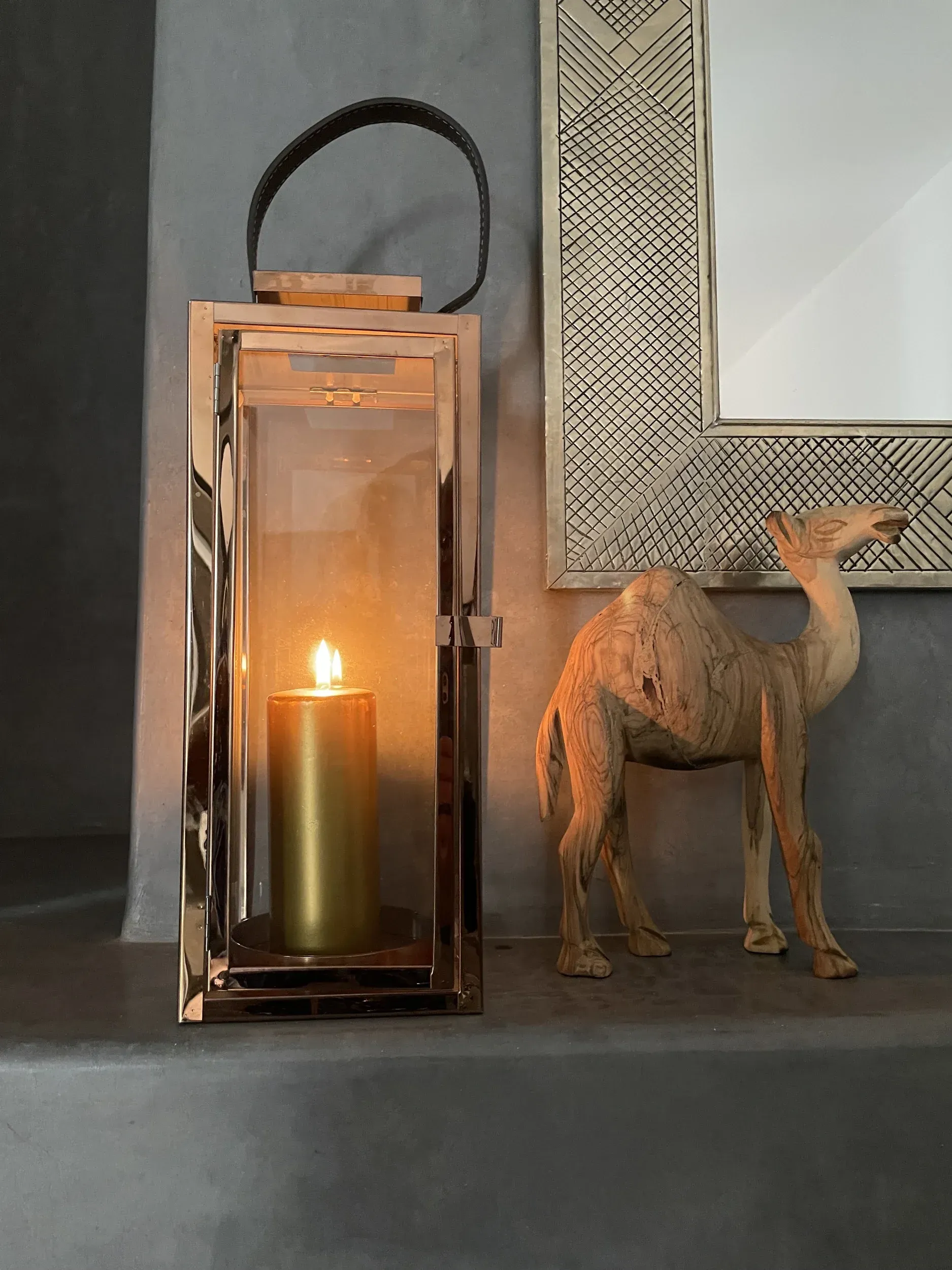 A candle is lit in a lantern next to a statue of a camel.