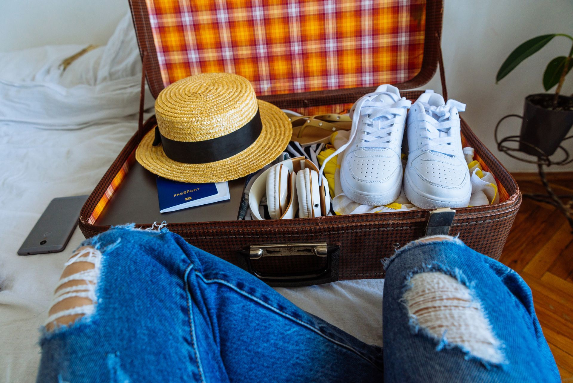 A person is sitting on a bed next to a suitcase filled with clothes and shoes.