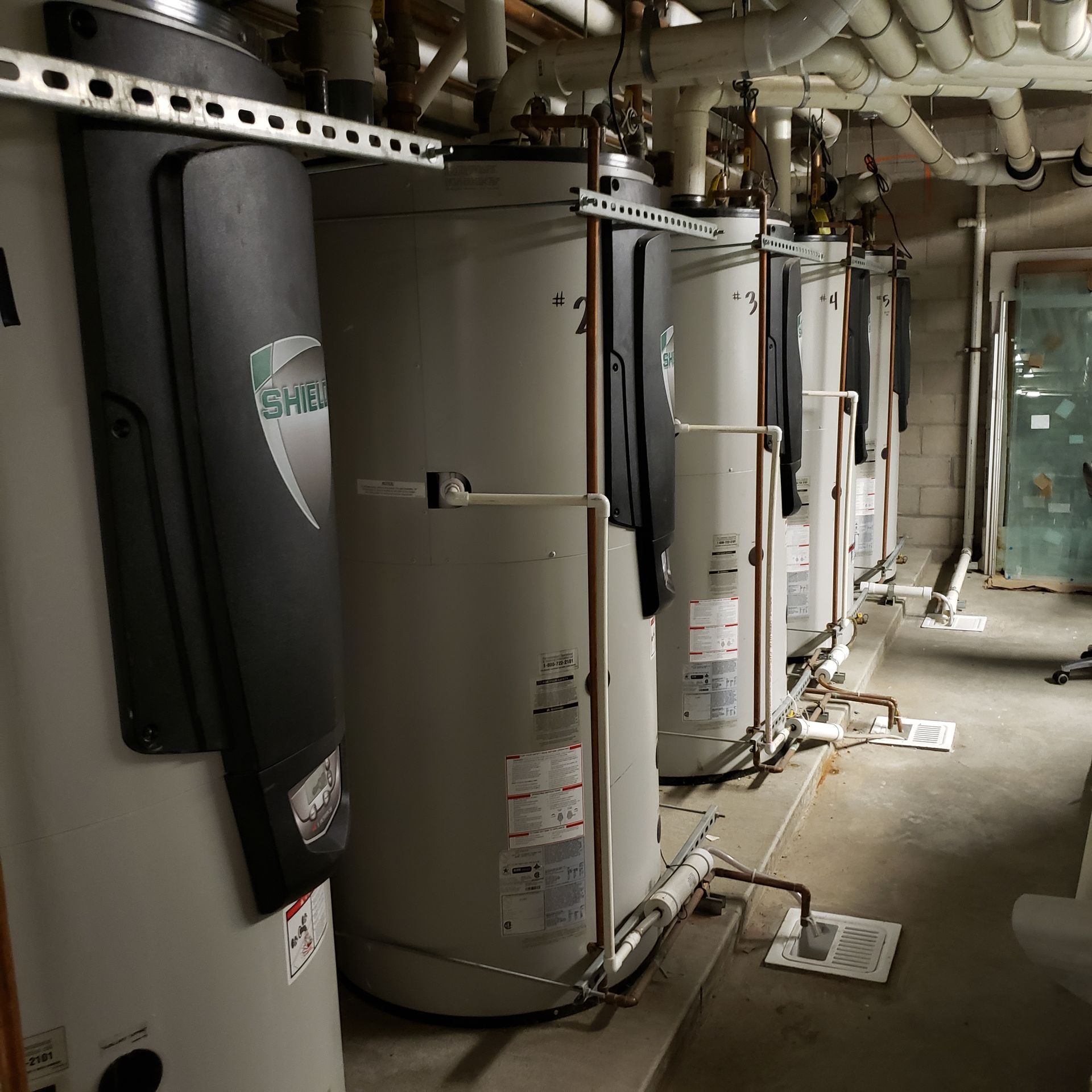 A row of tall, cylindrical water heaters in a utility room.