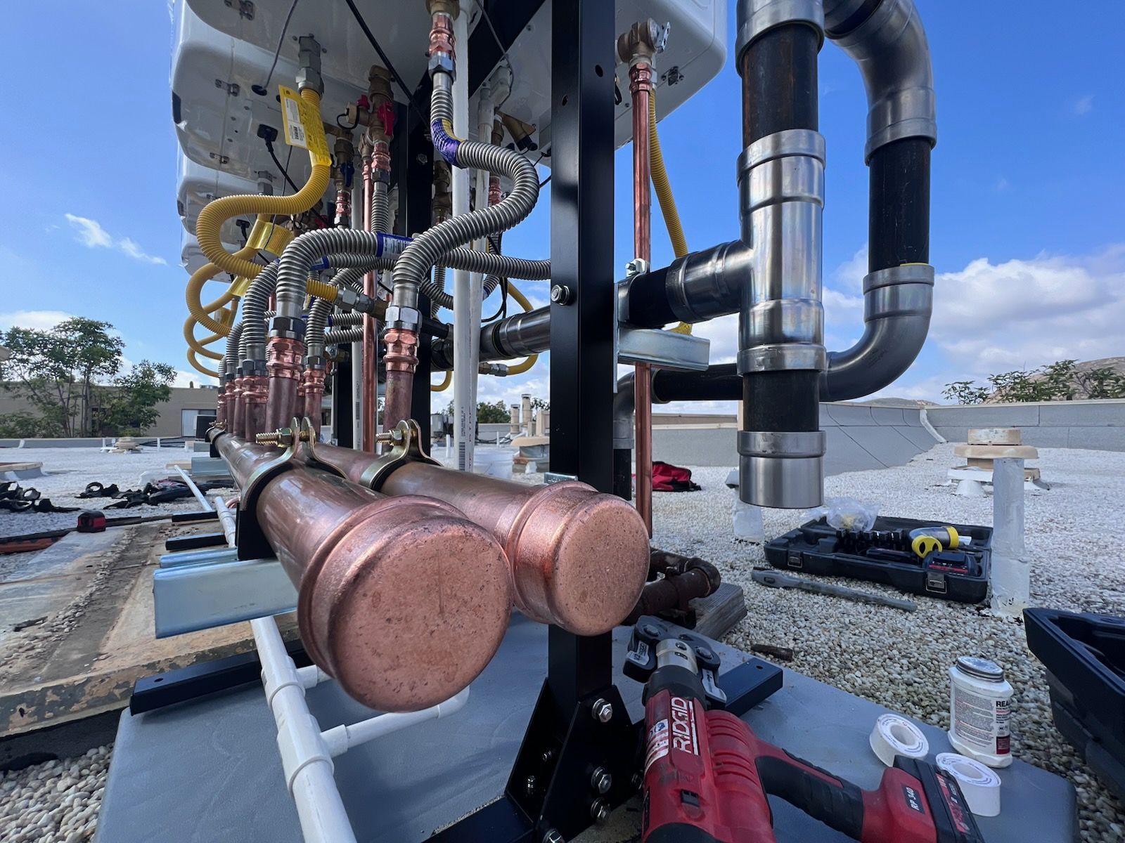 Plumbing system installation on a rooftop. Copper pipes and flexible hoses are connected to white fixtures.