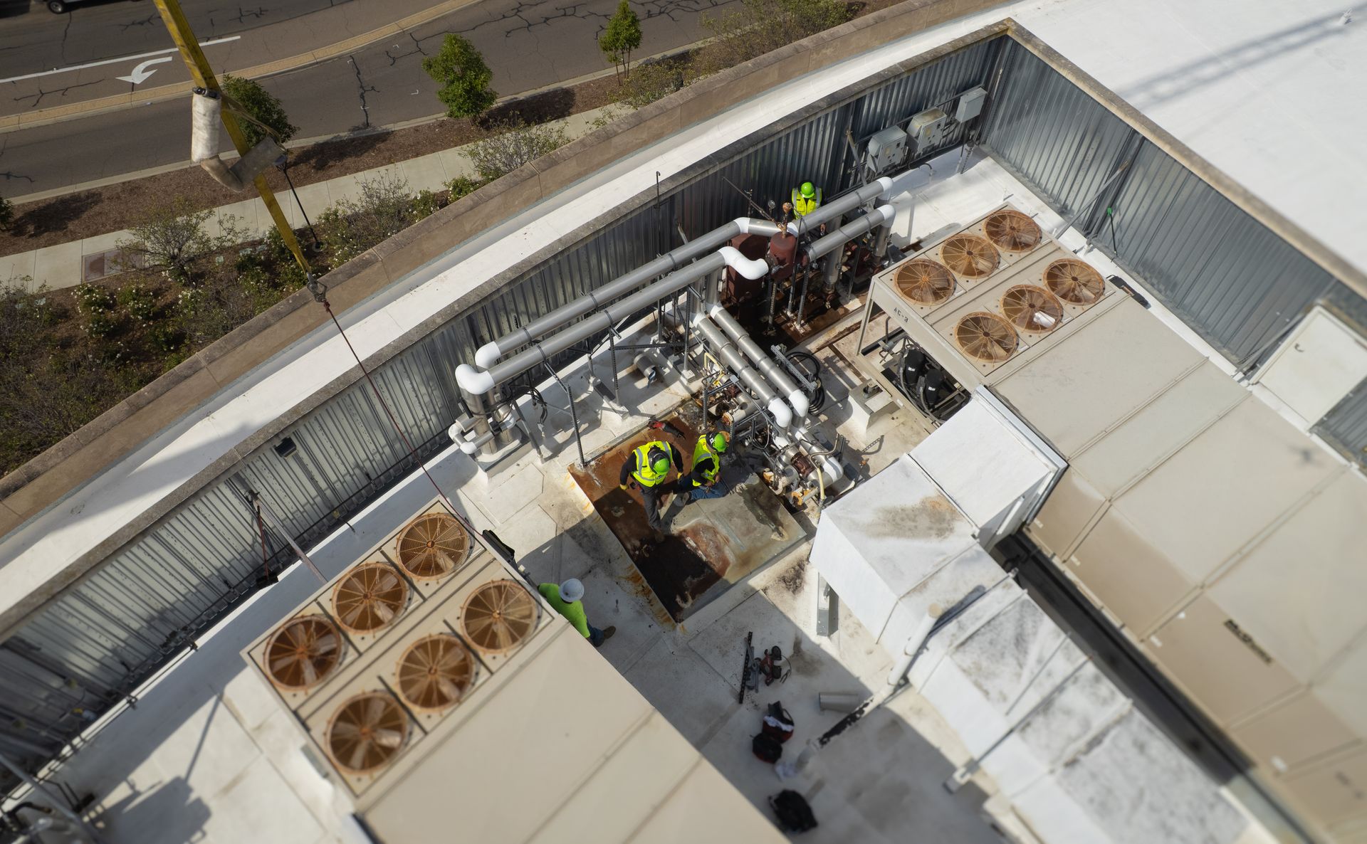 Aerial view of rooftop HVAC units and workers servicing equipment beside a street.