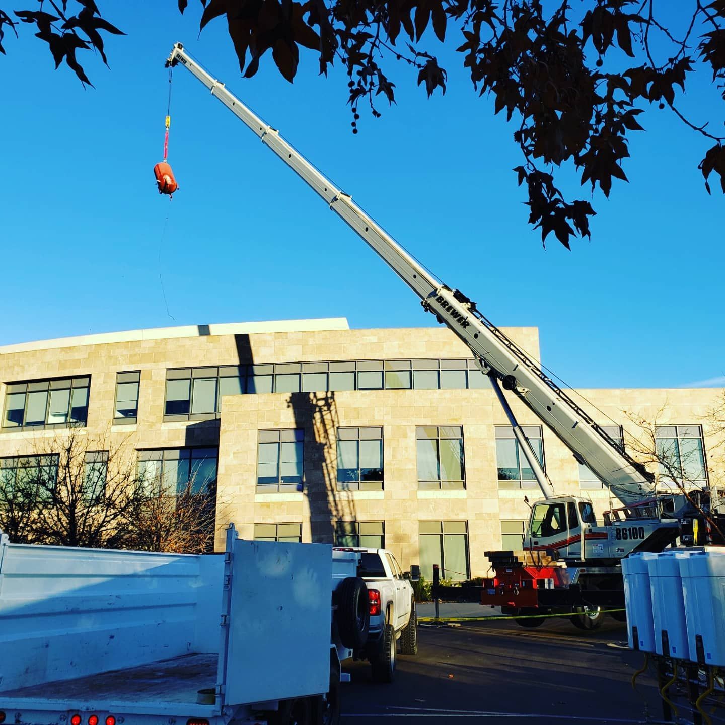 A crane lifting a boiler near a light-colored building. A truck and other equipment are in the foreground.