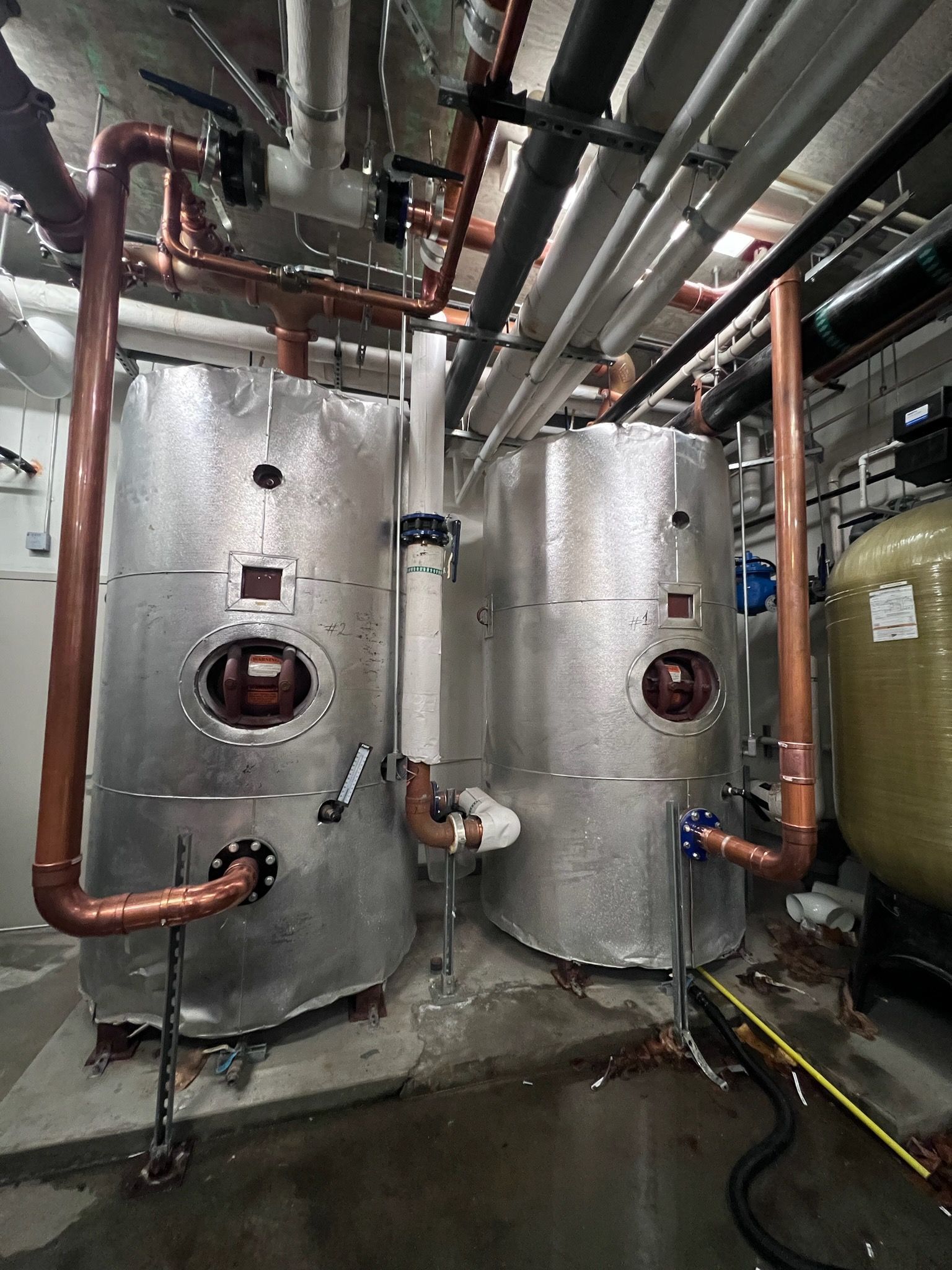Two large, commercial boilers with copper pipes in a utility room.