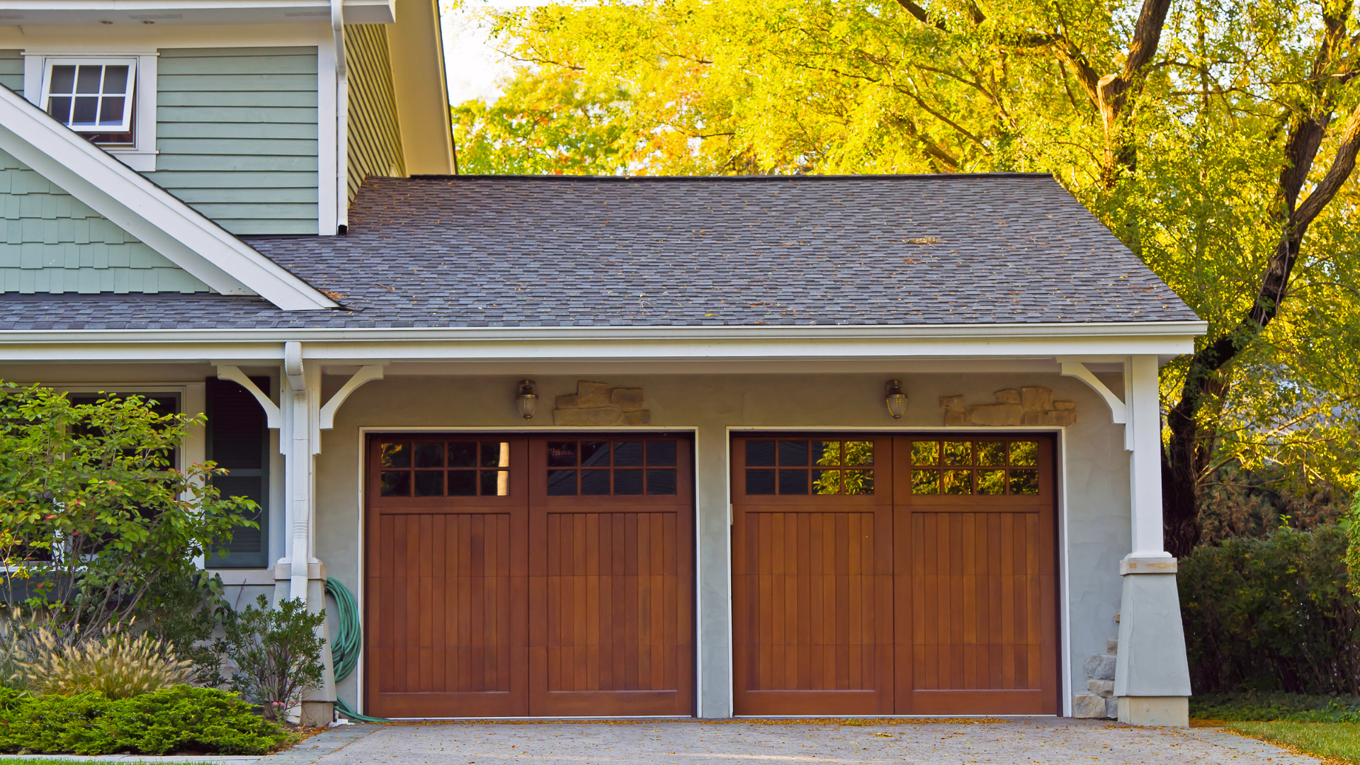 Brown garage doors under a gray roof, connected to a light green house.