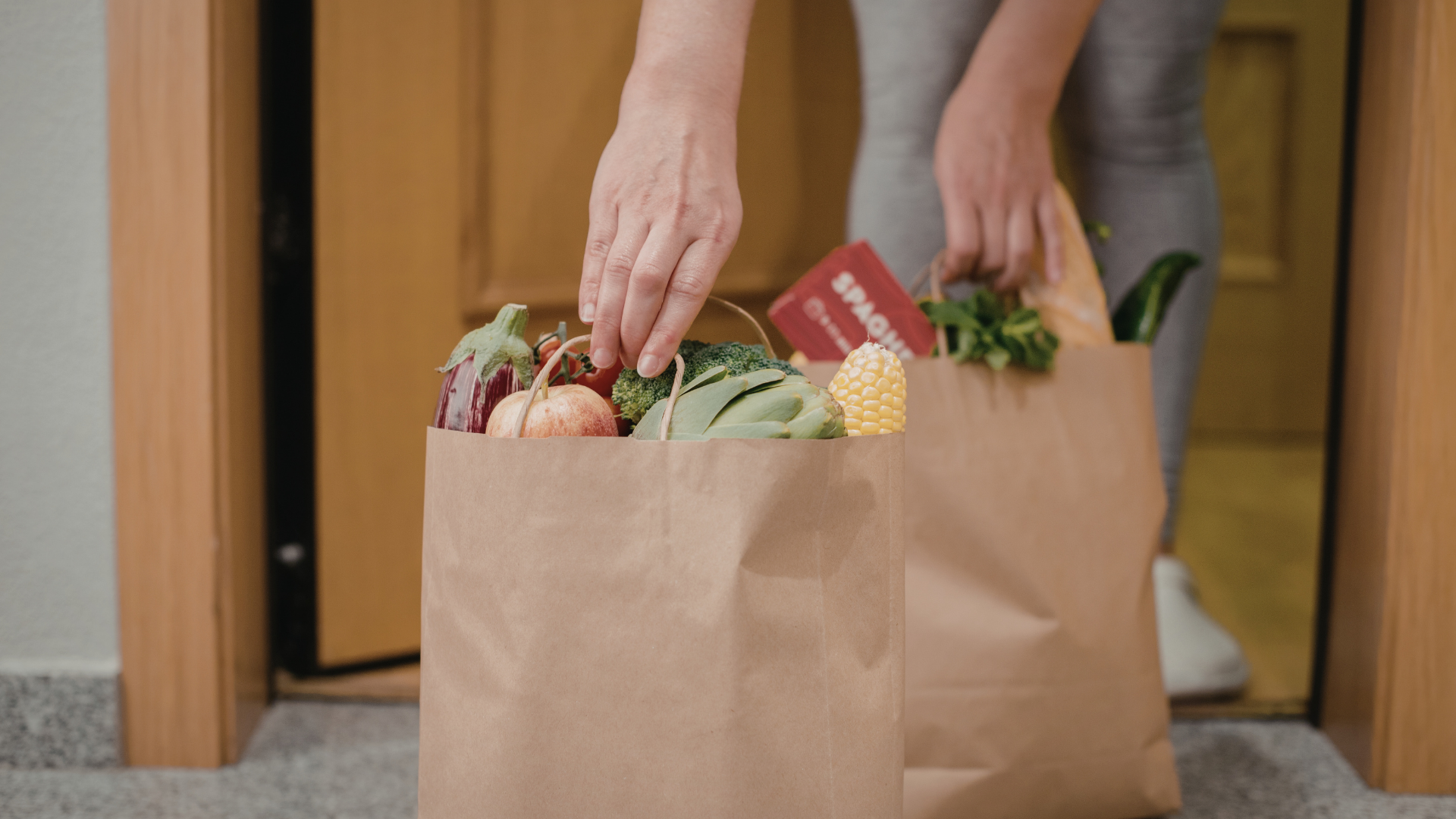 Person taking groceries out of brown paper bags by a door.