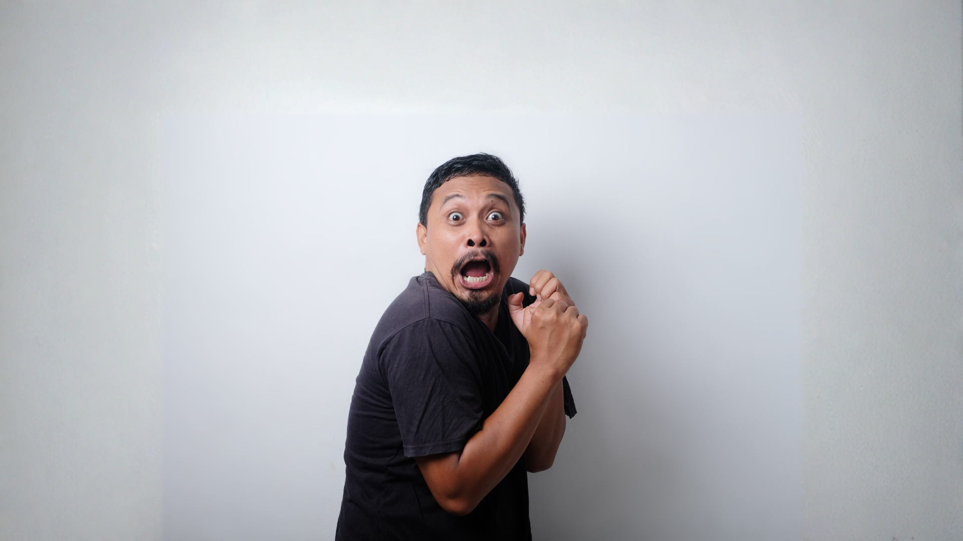 A person in a black t-shirt against a plain white background with an wide-eyed, shocked expression.