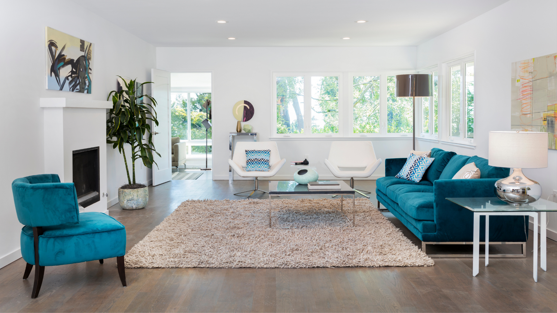 Bright modern living room with teal chairs, white sofa, large windows, and a shag rug