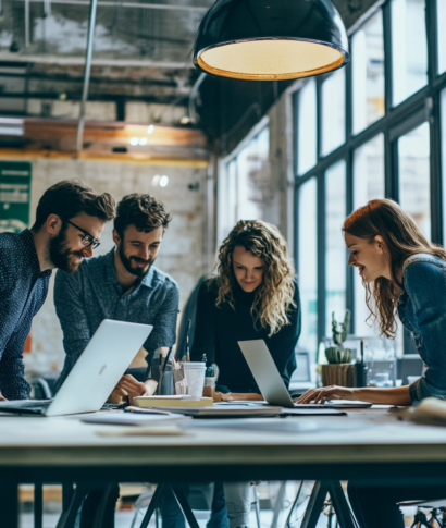 Four people collaborating around a table with laptops in a modern office.