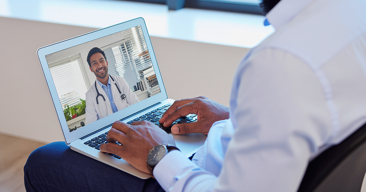 Man on laptop video calls with a smiling doctor wearing a stethoscope.