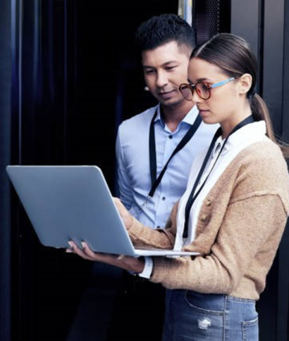 Two IT professionals looking at a laptop in a server room.