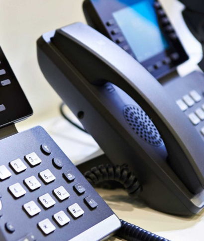 Close-up of three black office phones with buttons and handsets, on a white surface.