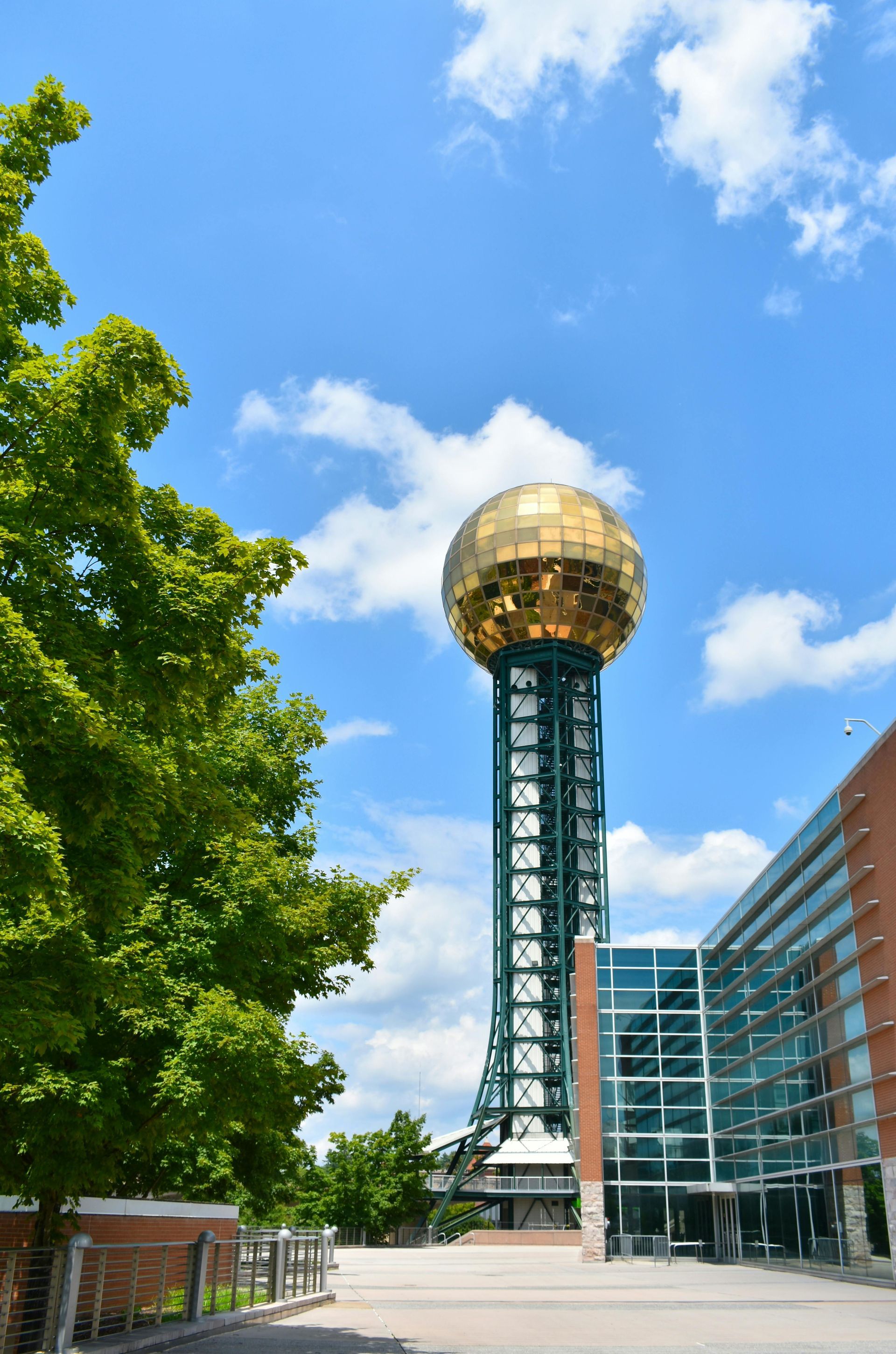The Sunsphere in Knoxville, Tennessee, a golden-domed tower, rises above a modern building under a sunny blue sky.