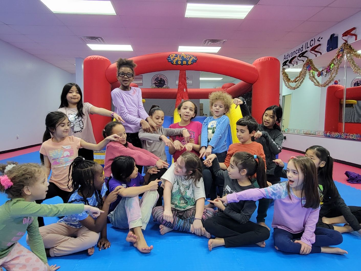 A group of children are sitting on the floor in front of a bouncy house.