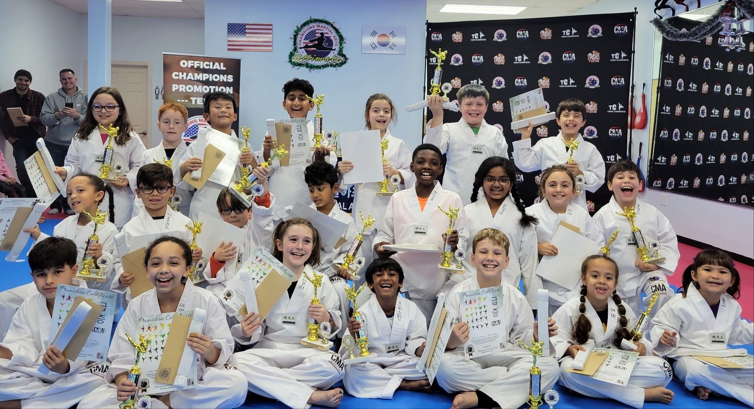 A group of children are sitting on the floor holding trophies.