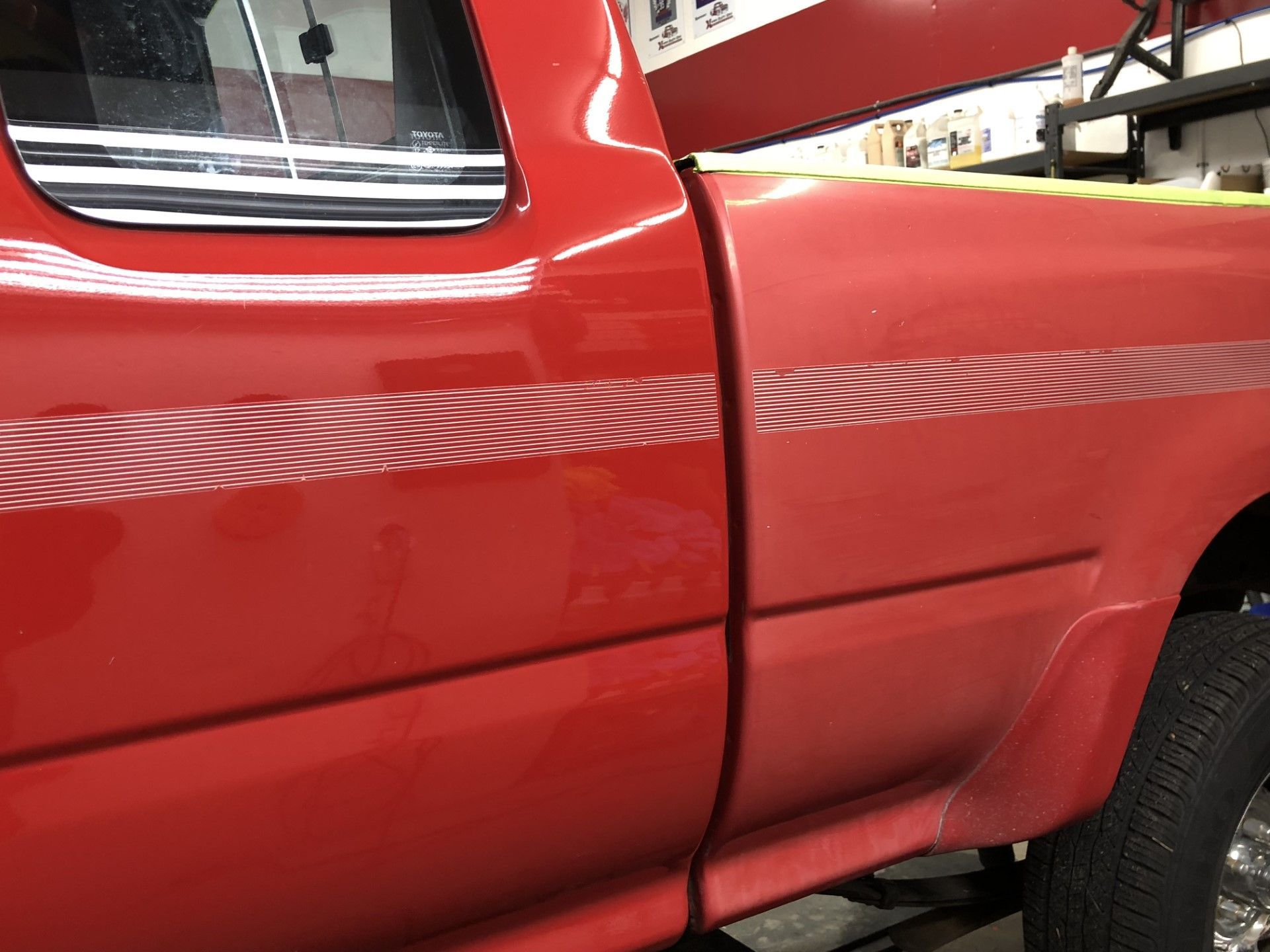Close-up of a red pickup truck door and side panel in a garage.