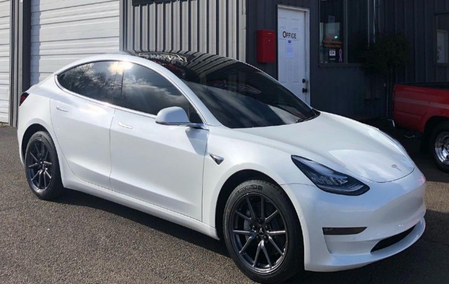 White Tesla Model 3 car parked outside a building with tinted windows and black rims.