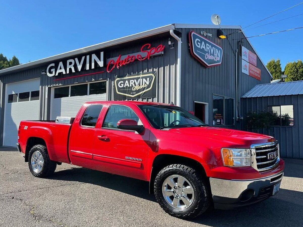 Red GMC Sierra pickup truck parked in front of a car dealership with a Garvin Auto Sales sign.