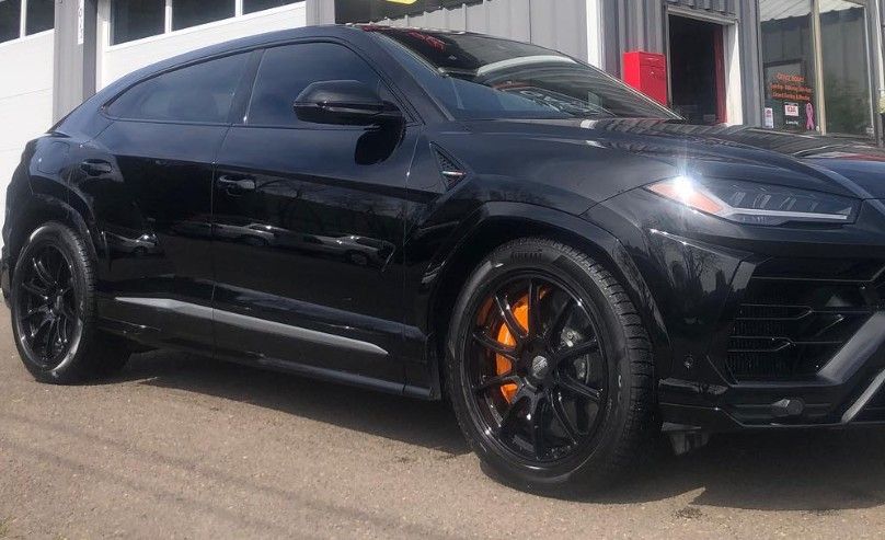 Black sports coupe with tinted windows and orange brake calipers parked outside a building