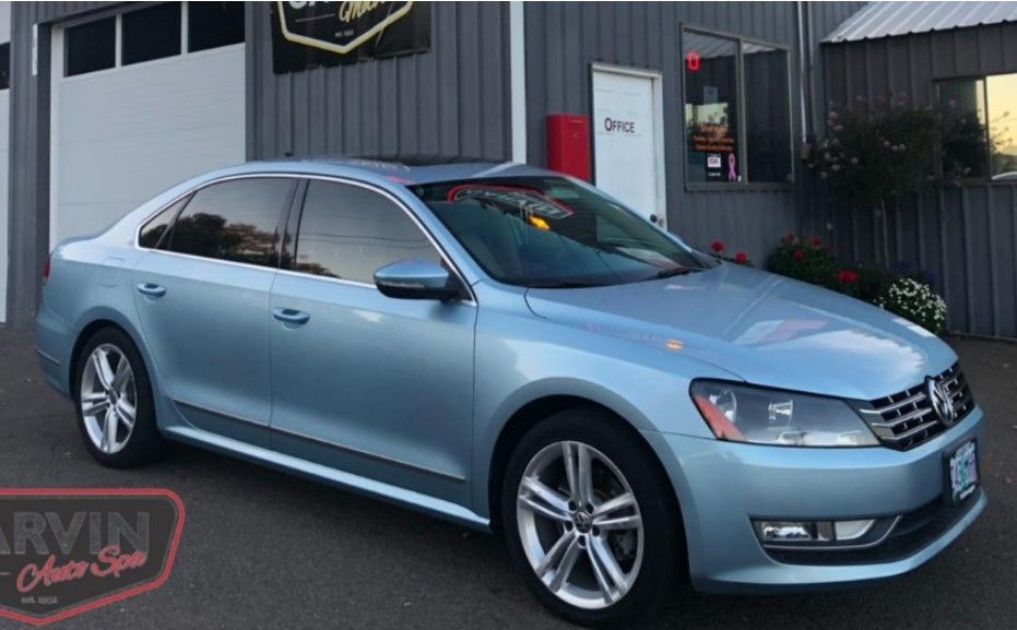 Light blue Volkswagen Passat sedan parked outside a building with tinted windows.