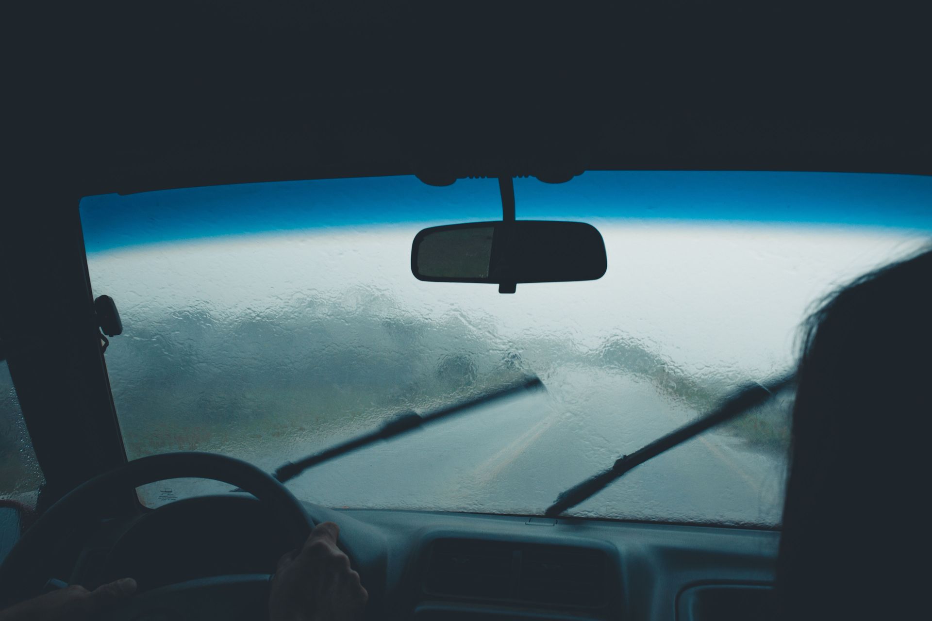 Driver’s view through a fogged windshield with wipers on during rainy conditions.