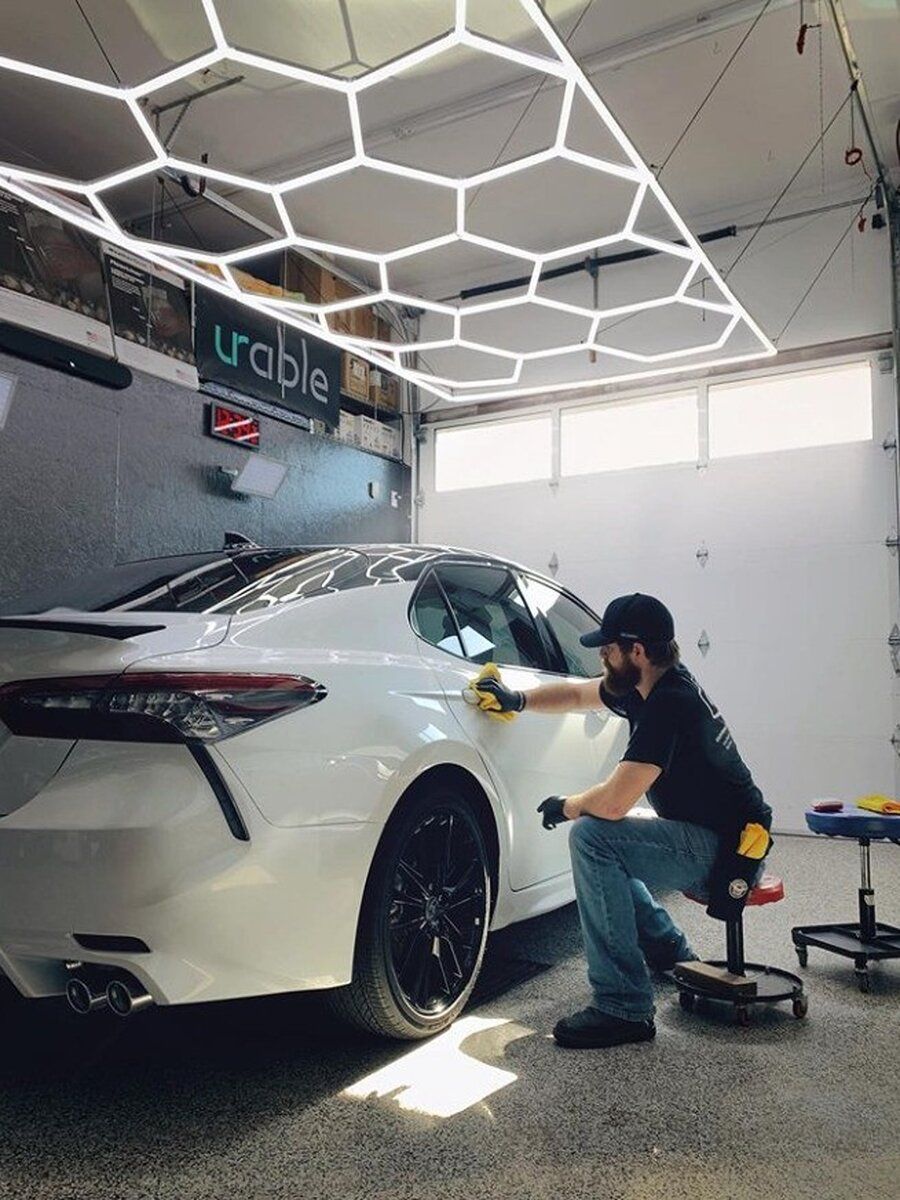 Person applying clear protective film to a car hood with a squeegee, indoors. The car is silver.